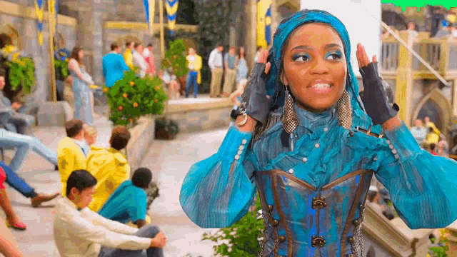 a woman in a blue and brown outfit is standing in front of a crowd of people .
