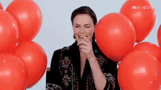 a woman is surrounded by red balloons and a marieclaire logo
