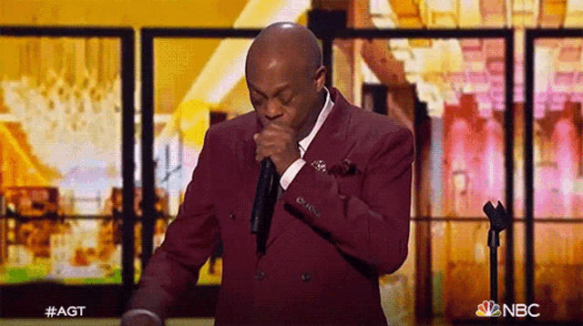 a man in a maroon suit is singing into a microphone on a stage .