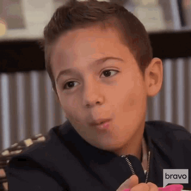 a young boy is sitting at a table with bravo written on the bottom of his shirt