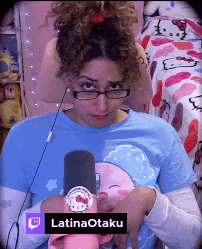 a woman wearing glasses and a hello kitty shirt is holding a microphone with the name latinaotaku on the bottom