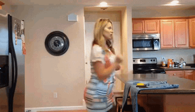 a woman is dancing in a kitchen with a clock on the wall that says 12:26