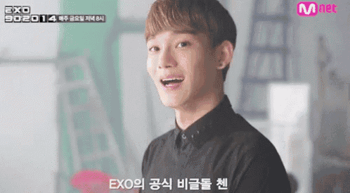 a young man in a black shirt is smiling in front of a mnet sign