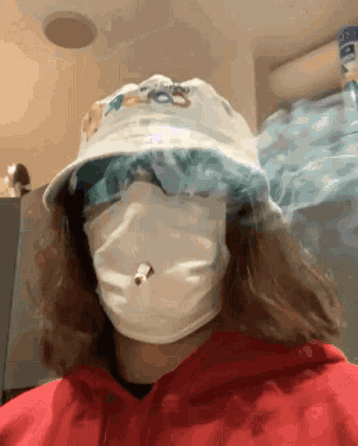 a person wearing a bucket hat and a face mask is smoking a cigarette .