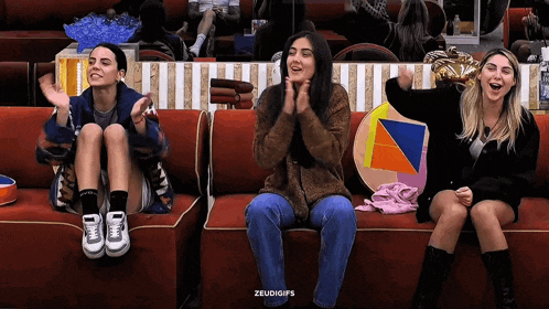three women are sitting on a red couch with their hands in the air and the words zeudigips written below them