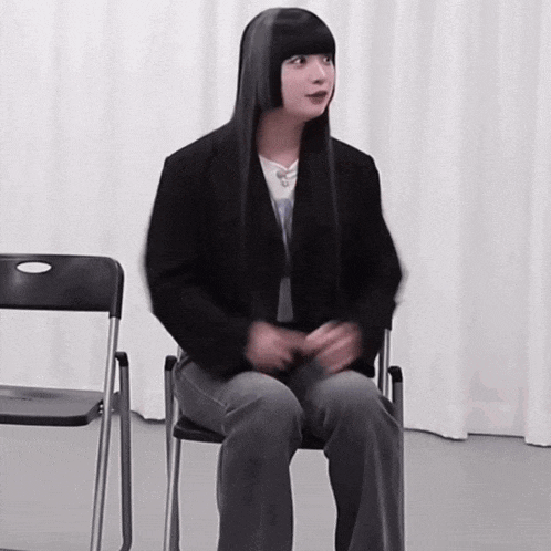 a woman with long black hair sits in a chair