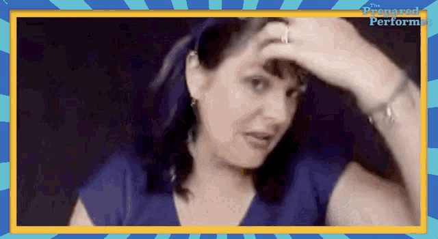 a woman in a blue shirt is holding her hand to her forehead in front of a blue and yellow striped background .