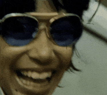 a woman wearing sunglasses is smiling and looking at the camera