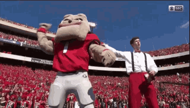a mascot is dancing in a stadium with two men .