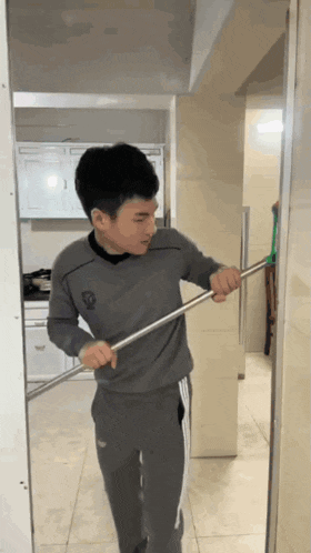a young man in a gray shirt is holding a mop
