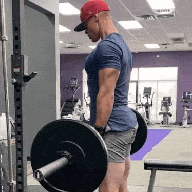 a man wearing a red hat is lifting a barbell with a plate that says ' rogue ' on it