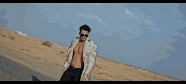a shirtless man wearing sunglasses and a fur coat stands next to a red car in the desert