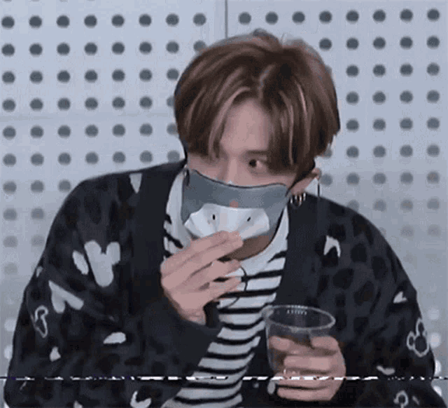 a young man wearing a mask is eating a snack and holding a glass of water .