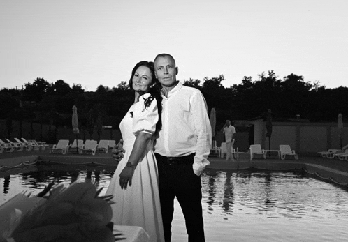 a black and white photo of a man and woman standing next to a swimming pool