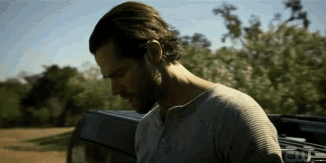 a man with a beard is standing in front of a car with a cw logo in the background