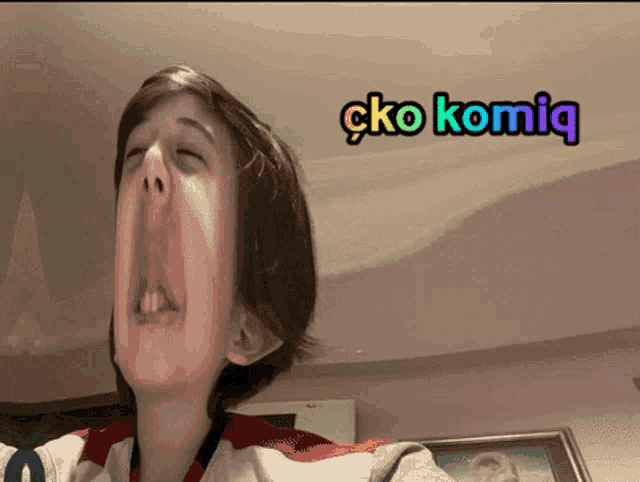 a young boy making a funny face with a sticker that says ' cko komiq ' on it