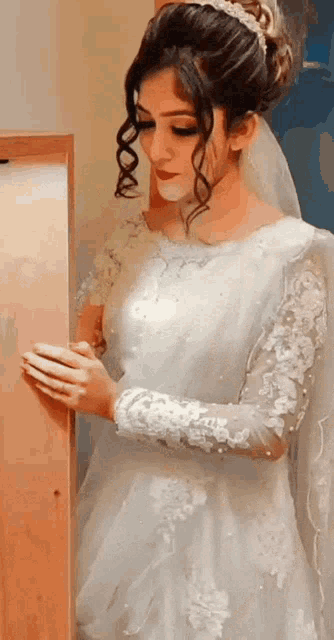a woman in a white wedding dress is standing in front of a wooden cabinet .