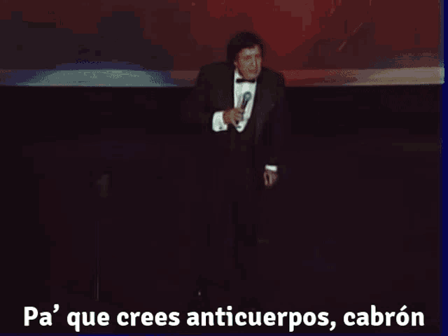 a man in a tuxedo is singing into a microphone with the words pa que crees anticuerpos cabron written below him