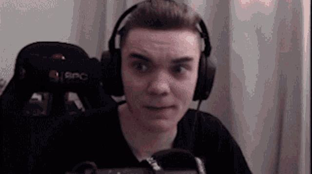 a young man wearing headphones and a black shirt is sitting in front of a microphone .