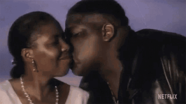a man and a woman are kissing in front of a purple sky .