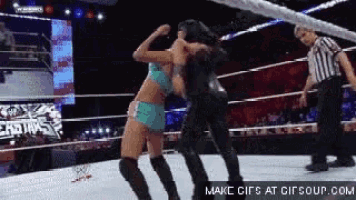 two women are wrestling in a ring with a referee in the background .