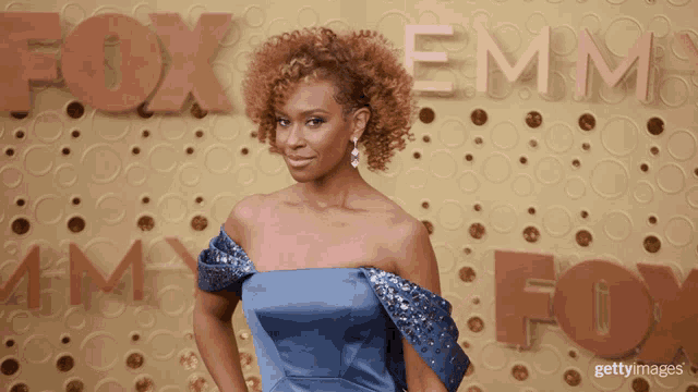a woman in a blue dress is standing in front of the fox emmy logo