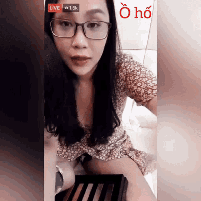 a woman wearing glasses is sitting on a bed in front of a sign that says live