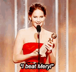 a woman in a red dress is holding a trophy and speaking into a microphone while saying i beat meryl .