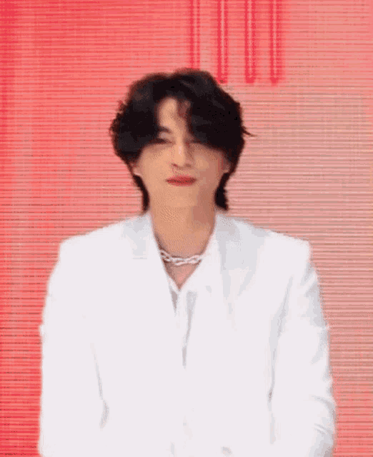 a man wearing a white suit and a necklace is standing in front of a red background .