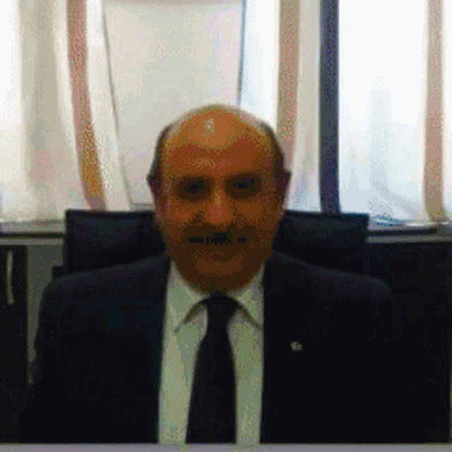 a bald man with a mustache is sitting in front of a window