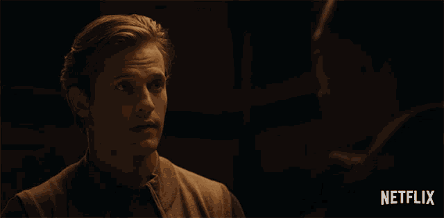 a man in a suit and tie is talking to another man in a dark room with a netflix logo in the corner