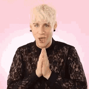 a young man with blonde hair is wearing a black lace shirt and praying with his hands together .