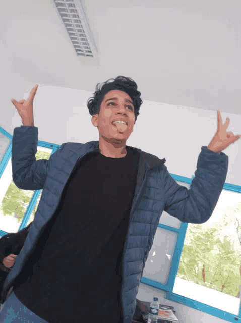 a young man in a black shirt and blue jacket is making a devil horns gesture