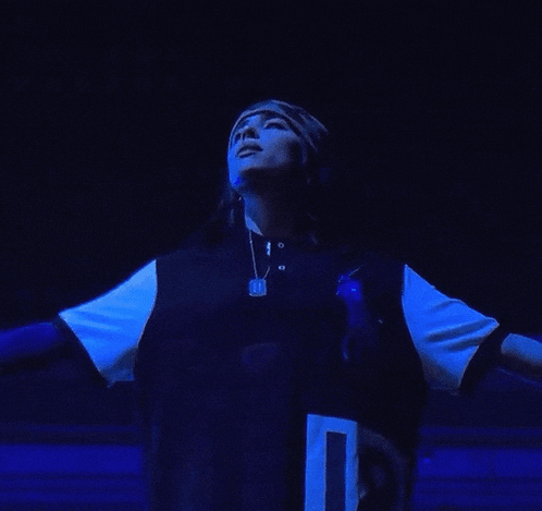 a woman is standing in the dark wearing a blue shirt and a hat .