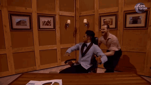 two men are dancing in a room with a dancing in brass logo