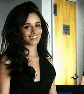 a woman in a black dress is smiling and standing in front of a yellow door .