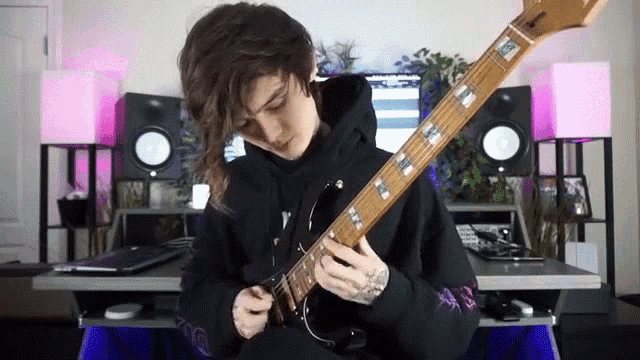 a person in a black hoodie is playing a bass guitar