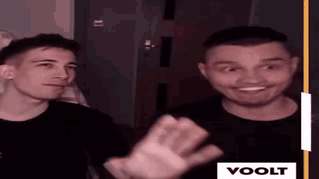 two men are sitting next to each other and one of them is smiling and waving at the camera .