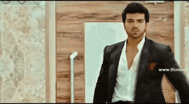 a man in a black suit and white shirt is standing in front of a wooden door .