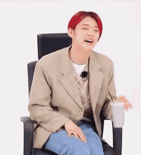 a young man with red hair is sitting in a chair holding a cup and smiling .