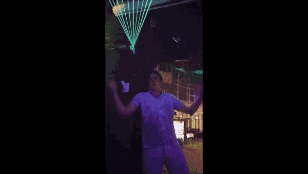 a man in a white shirt is dancing in a club with a green laser beam behind him .