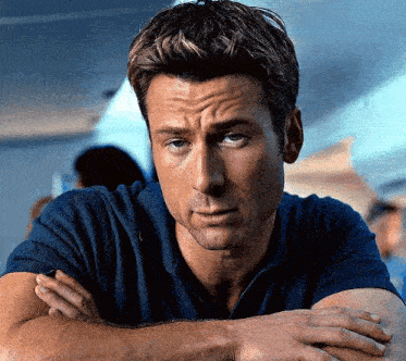 a man in a blue shirt has his arms crossed and is looking at the camera