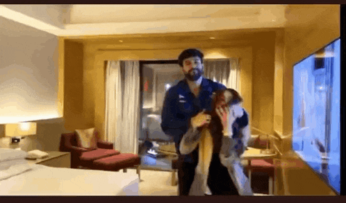 a man is holding a woman in his arms in a hotel room in front of a television .