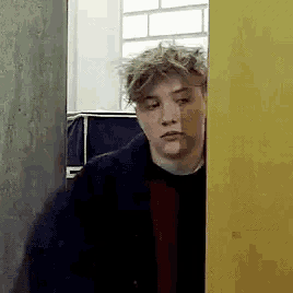 a young man is standing behind a yellow door .