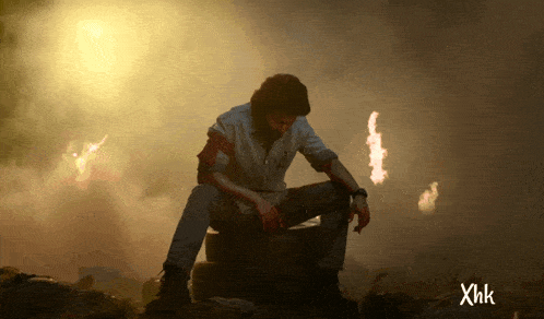 a man sits on a tire in a dark room with xhk written on the bottom