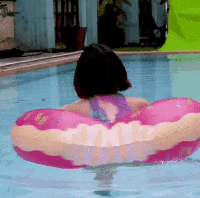 a woman is floating in a swimming pool with a pink donut float .