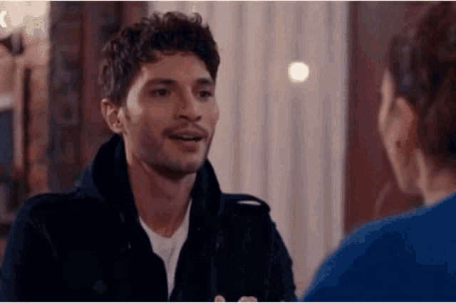 a man in a black jacket is talking to a woman in a blue sweater .