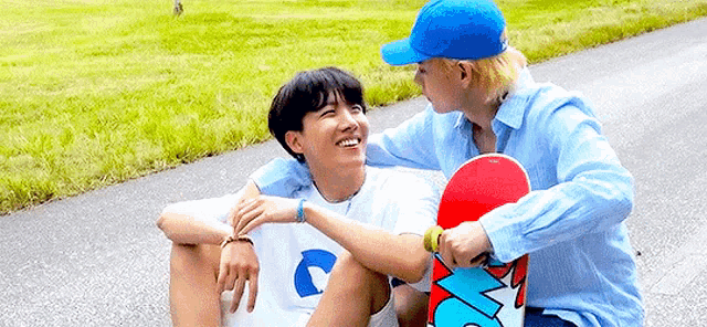 two young men are sitting on the side of a road holding a skateboard .