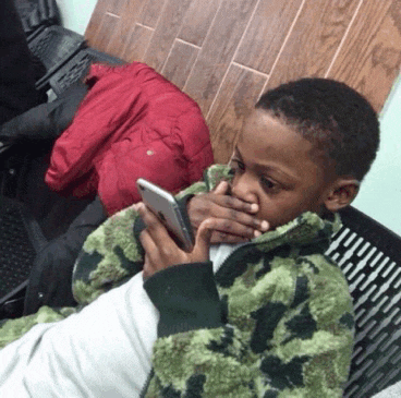 a young boy covering his mouth with his hand while looking at a cell phone