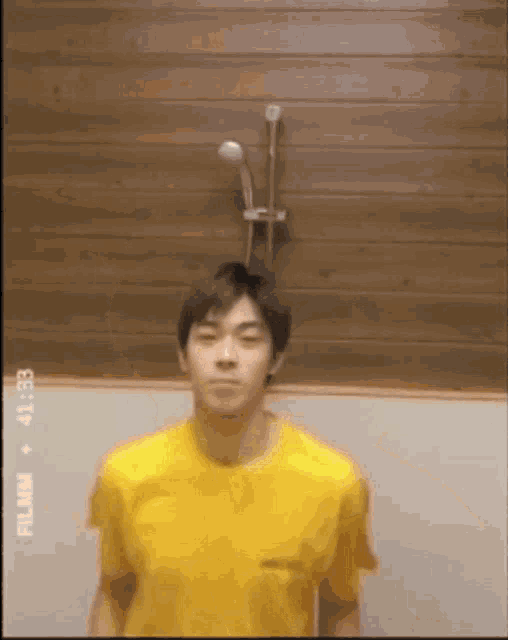 a man in a yellow shirt is standing in front of a shower head